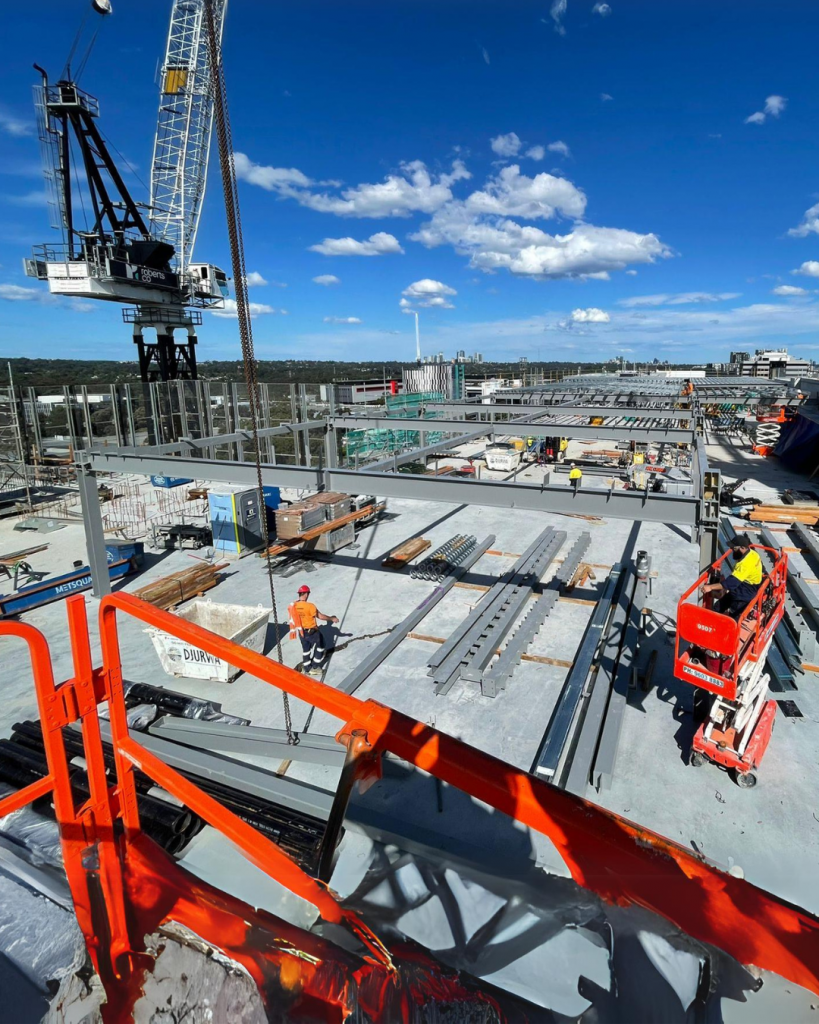 Hard Bakka Rigging team performing steel installation on a high-rise project in Sydney under clear blue skies with cranes and rigging equipment on site.