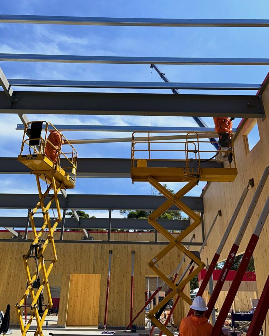 Steel installation at Gonzalez Steel project in Warriewood, with riggers using scissor lifts to position beams for structural assembly.