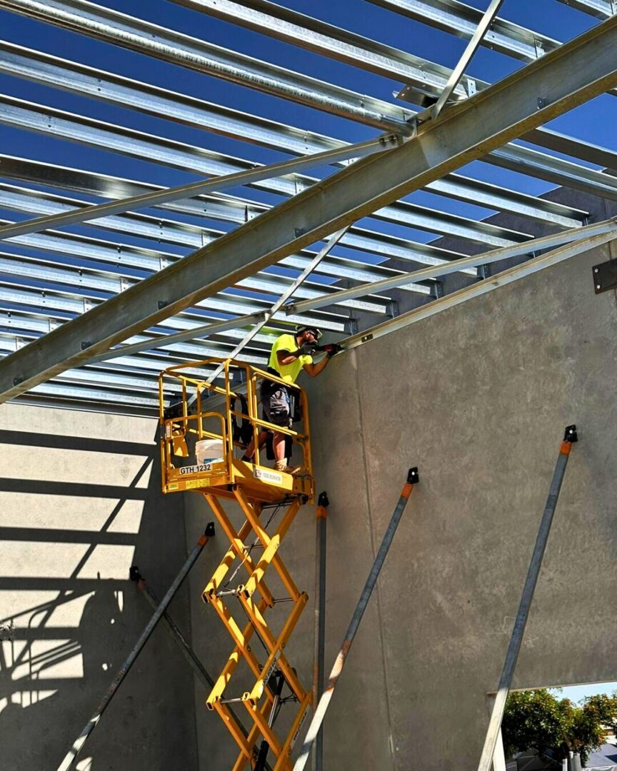 Rigger working on steel canopy installation at BP Milperra using a scissor lift under blue sky