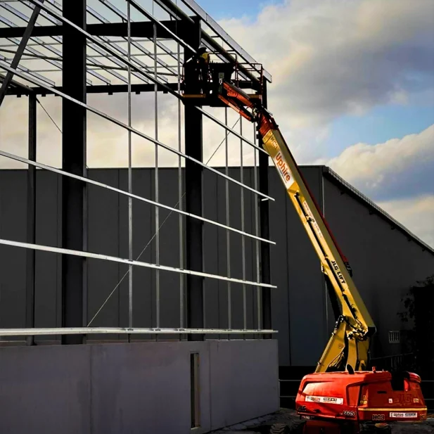 Hard Bakka Rigging team member working on elevated steel framework installation using a boom lift.